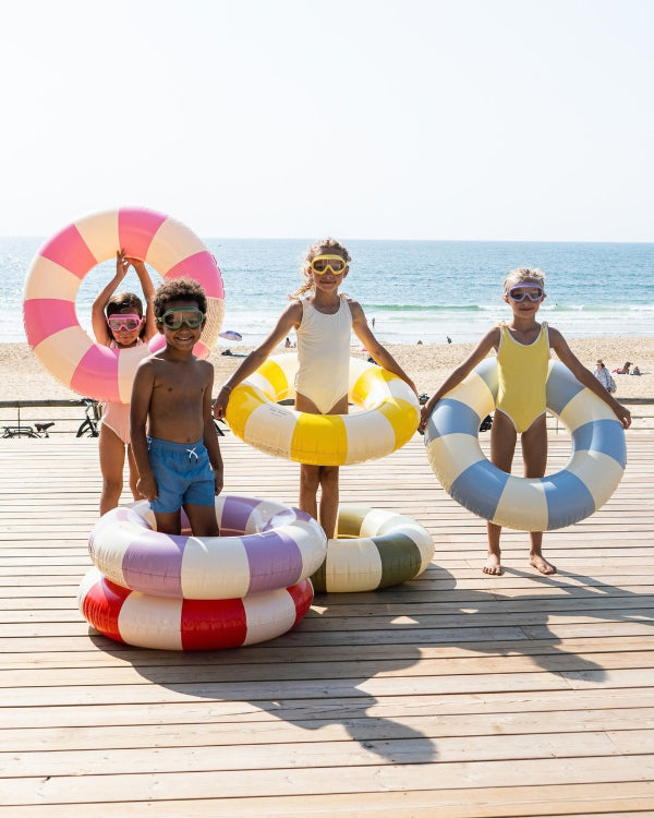 Kids in matching swimwear holding striped swim rings on a beach boardwalk