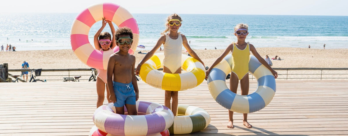 Kids in matching swimwear holding striped swim rings on a beach boardwalk