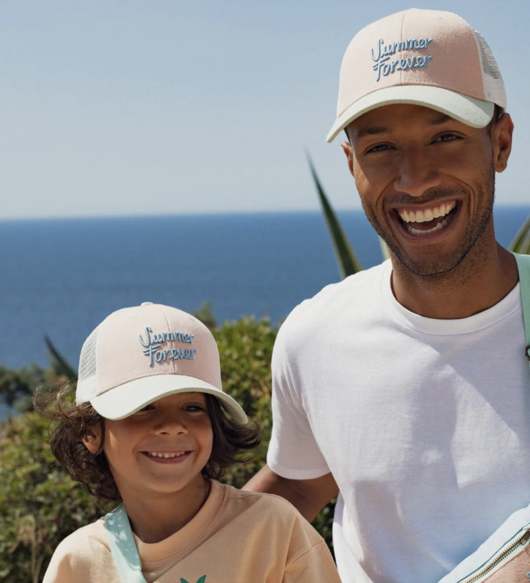 Father and son in matching Chamaye trucker caps by the sea
