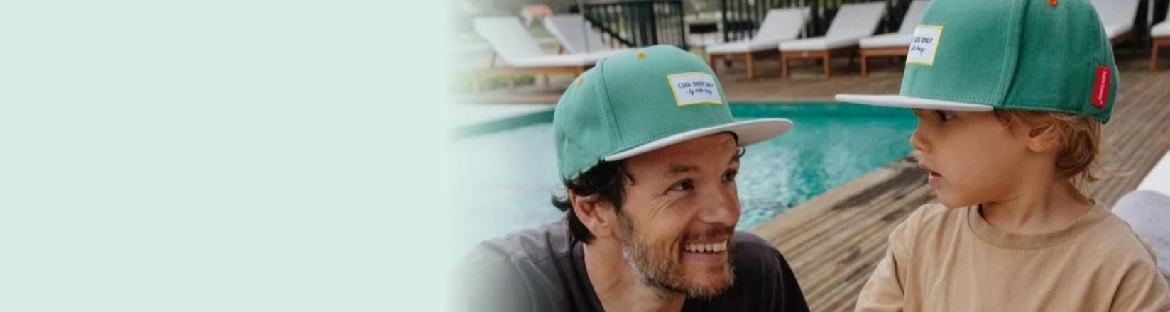 Dad and son in matching green caps by the pool