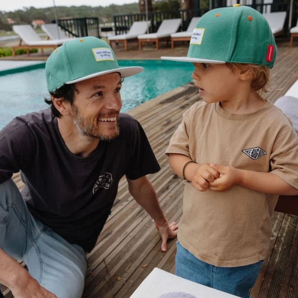 Father and son in matching green caps by the pool